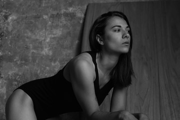Black and white horizontal shot of Caucasian woman with shot brunette hair, looking thoughtfully aside, posing indoors, put hands on wooden table. Fashionable shot of young sensual female model.