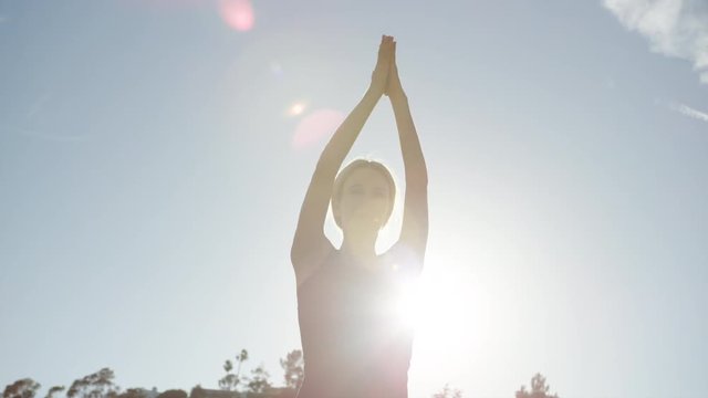 SLOW MOTION video of young woman doing yoga outside with strong sunlight behind her