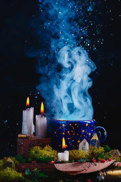 Alchemist workplace with burning candles, smoke, crystals, moss and potion bottles. A magical concept with copy space. Handmade ceramic cup with constellations and stars in a dark still life.