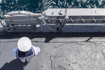 sailor in white uniform standing peacefully on the deck of a warship. A military warship and...