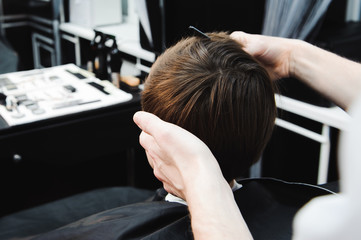 Young handsome barber making haircut of cute boy in barbershop