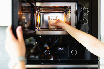 Woman warming a glass of milk in the microwave.