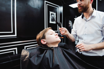 Cute little boy is getting haircut by hairdresser at the barbershop