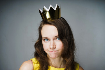 sad young blue-eyed girl looks into the camera and thinks about something, on her head a golden...