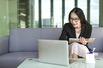 Young Asian businesswoman in suit and sweet dress working with laptop at office, professional working proficiency with smile and happy.