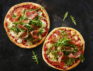 Pizza with ham and rocket on dark ground