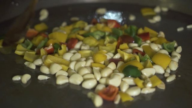 Chef cooking garlic and peppers on hot pan close up. Process preparing food in restaurant kitchen. Cook stewing vegetable garlic and bulgarian pepper in oil at pan.