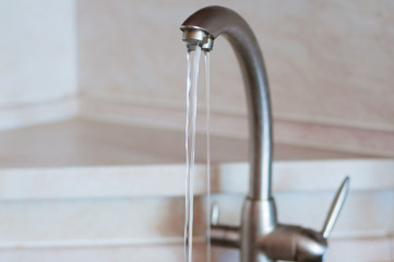 Water running from a silver tap with a filter part with a shelf on the background. Concept of water consumption