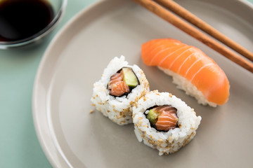Lachs Nigiri und Inside Out California Sushi mit Avocado, Sojasauce und Holz Stäbchen auf Porzellan Teller