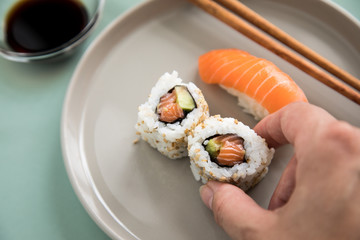 Frau isst Lachs Nigiri und Inside Out California Sushi mit Avocado und Sojasauce mit Fingern