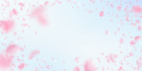 Fototapeta na wymiar Sakura petals falling down. Romantic pink flowers vignette. Flying petals on blue sky wide backgroun