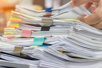 Teacher hands is searching for student's homework assignments archive with colorful paper clips on table to make a check and inspect. Stack of paperwork and reports. Education and business concept.