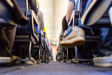 Naklejka premium Low agle view of passenegers commercial airplane aisle with passenegers sitting on their seats while flying.