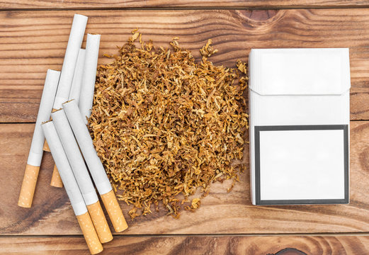 Pile of dry cut tobacco with cigarettes and pack of cigarettes on wooden table. Top view.