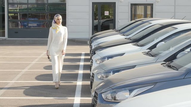 Buying or renting a car concept. Young Muslim woman chooses a car to buy or rent