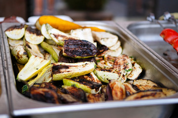 Fried vegetables: courgettes, aubergines in a container on open kitchen food festival event. Street food and outdoor cooking concept.