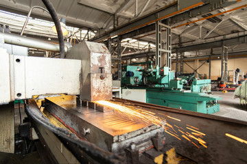 Fototapeta premium Metal parts on a flat grinder are treated with an abrasive wheel, sparks fly from under the circle, wide-angle photos.