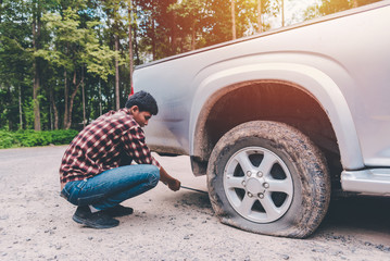 Young man is changing tires on car the road because he was repairing in the bright sunlight.