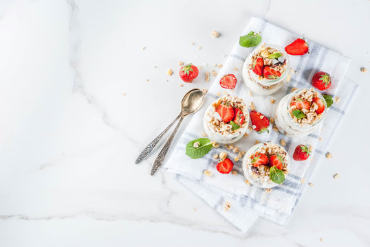 Healthy summer breakfast idea, homemade layered parfe dessert in small jar with granola, yoghurt and strawberry, dark background copy space above
