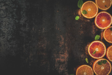 Fresh raw blood oranges, halves, with mint, on dark rusty background copy space top view