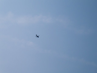 Looking up from the ground at the silhouette of a flying plane under blue sky taken from below at day. Plane flying from left to right.