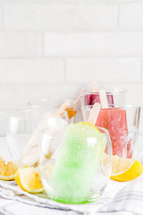 Summer party food ideas, frozen boozy alcohol cocktails popsicles - Prosecco, Vodka lime mojito, Champagne, Bellini, Margarita, Negroni etc white marble table copy space