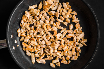 Pieces of chicken fried in a frying pan, top view