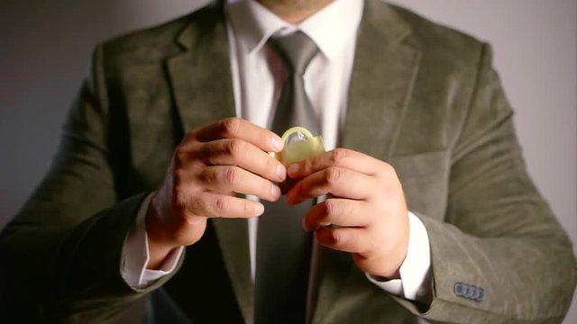Elegant business man in a white shirt with a tie and a jacket pulls a condom out of the package. sign all right and good