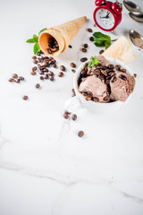 Homemade coffee ice cream, served with coffee beans and mint leaves, with ice cream cones and spoons in the picture. White marble background,
