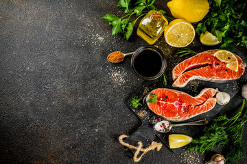 Raw salmon fish steaks with lemon, herbs, olive oil, ready for grill, slate cutting board, dark rusty background copy space