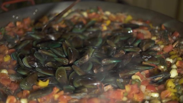 Chef cooking seafood mussels and shrimps with vegetables in paella pan close up. Process preparing spanish food in restaurant kitchen. Cook stewing vegetables with seafood for spain paella at pan.