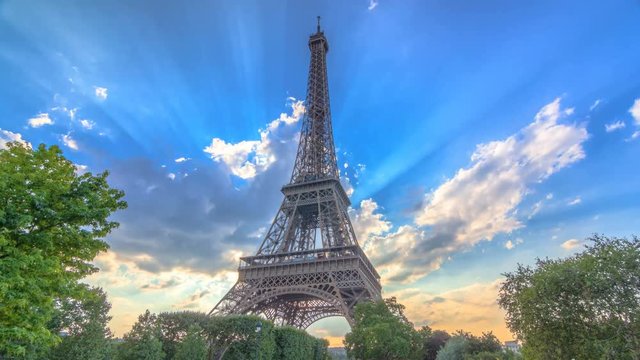 The Eiffel tower with warm rays of light in clouds during sunset timelapse hyperlapse.