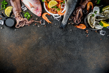Fresh raw seafood squid shrimp oyster mussels fish with spices of herbs lemon on dark rusty background copy space top view
