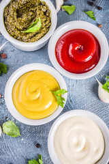 Set of four classic sauces - ketchup, mayonnaise, mustard, pesto - with herbs and spices. Blue concrete background top view copy space
