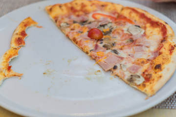 half eaten pizza with ham and mushrooms on white plate, selective focus