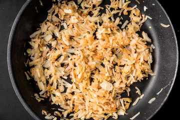Sliced onions are fried in a frying pan, top view