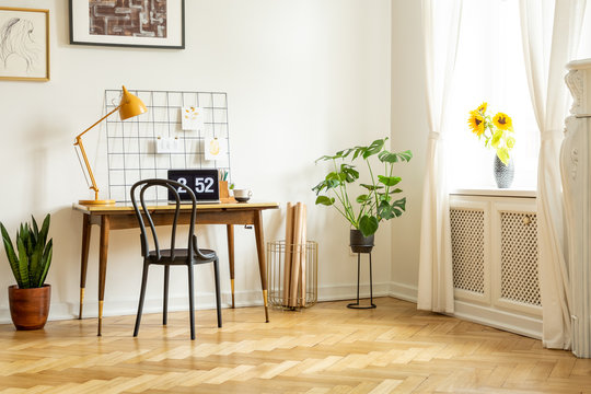 Spacious home office interior with a desk, chair, yellow lamp, plant and sunflowers. Real photo
