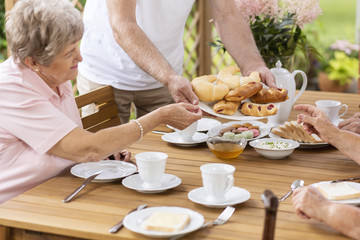 Person sharing food with elderly woman during breakfast in the terrace