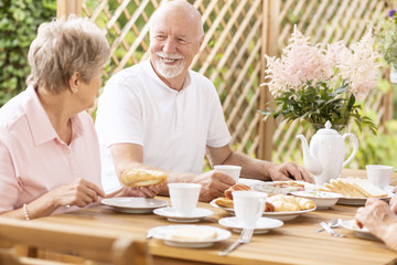 Smiling senior man eating breakfast with elderly woman on the terrace during summer