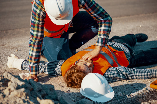 Worker in white helmet checking life functions of the injured during roadworks