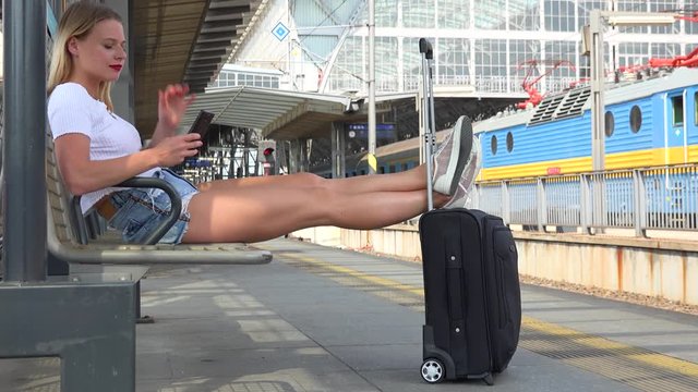 A young beautiful woman works on a smartphone on a train station platform