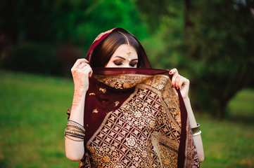 Portrait of beauty Indian model with bright make-up who hiding her face behind the veil. Young...