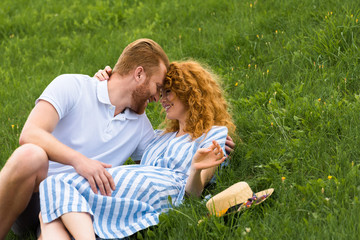 Fototapeta premium smiling redhead couple looking at each other face to face on grassy meadow
