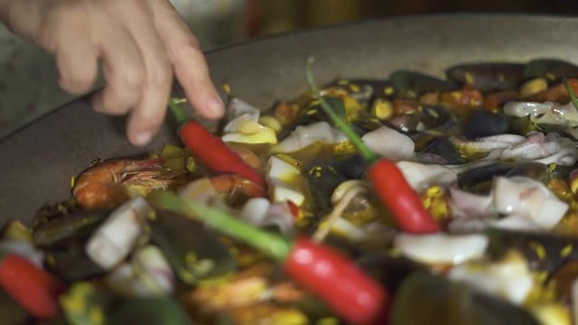 Chef cook cooking spanish paella with red hot peppers and fresh seafood in pan close up. Preparation traditional spain paella with mussels, shrimps, calamari and vegetables in pan.