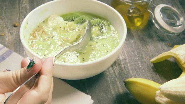 Female hand holding a tablespoon eating banana kiwi smoothiebowl