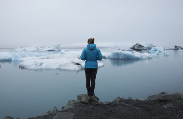 Fototapeta na wymiar A woman is looking the panorama of Jokulsarlon Glacier Lagoon in Iceland during an hike in a cloudy day. The ice and icebergs are floating in the sea