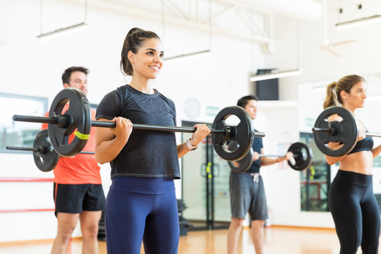 Woman Smiling While Lifting Barbell In Health Club