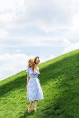 beautiful redhead woman holding straw hat on grassy hill
