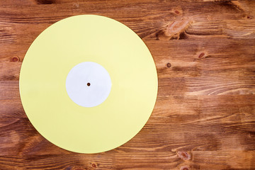 Yellow color vinyl record on brown wooden background