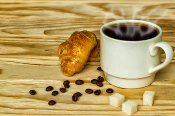 White cup with coffee and croissants on a wooden background, selective focus. The concept of breakfast.